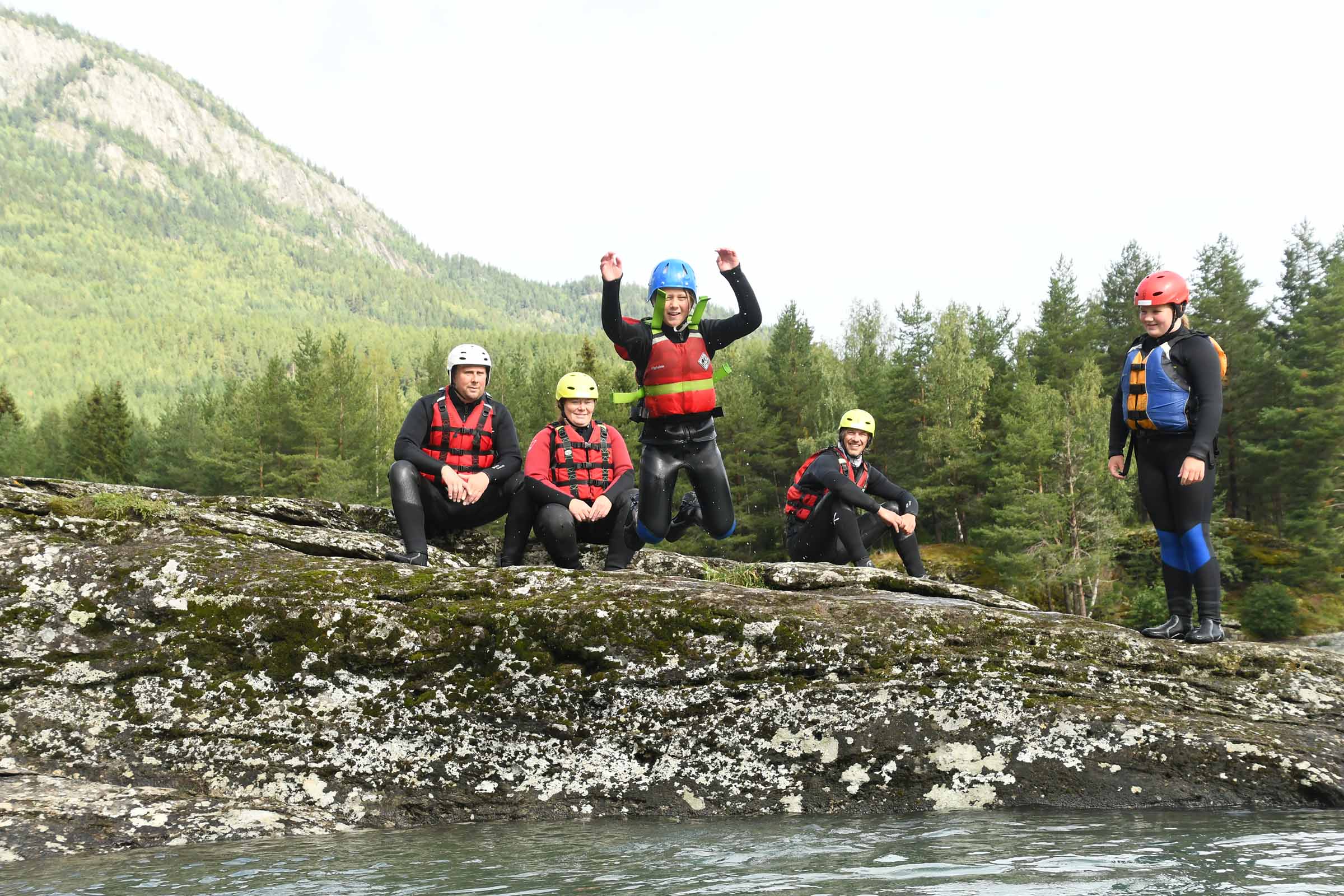 Familie sitter med våtdrakter på et berg langs med elven